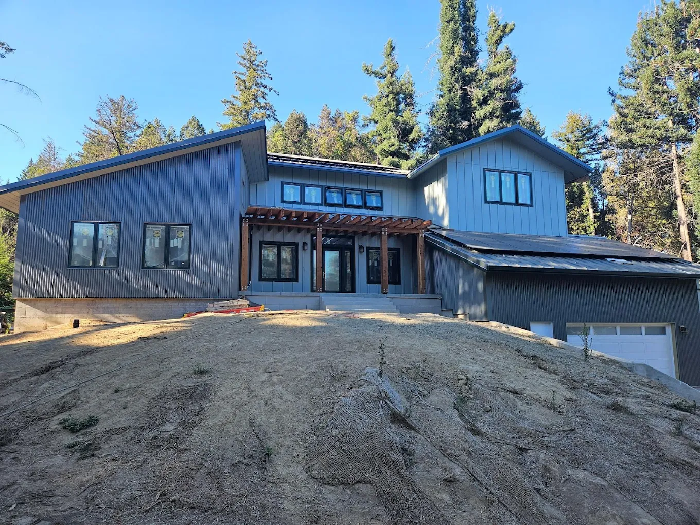 A finished custom home by SB Construction with gray siding and a wood-accent entry on a wooded hillside.